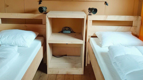 Twee eenpersoonsbedden met wit beddengoed, gescheiden door een houten kast bij Glampingtent Dreamer, Molengroet.