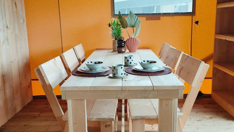 Table à manger en bois pour quatre avec vaisselle et plantes dans la Glampingtent Dreamer à Molengroet, Pays-Bas.