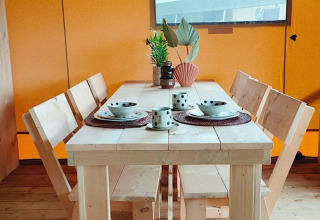 Table à manger en bois pour quatre avec vaisselle et plantes dans la Glampingtent Dreamer à Molengroet, Pays-Bas.