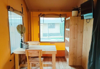 Indretning af Glampingtent Kompact ved Molengroet, Nederlandene, med træmøbler og vindue.