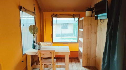 Indretning af Glampingtent Kompact ved Molengroet, Nederlandene, med træmøbler og vindue.
