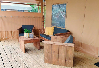 Zona de estar exterior en Glampingtent Kompact en Molengroet, Países Bajos, con muebles de madera y cojines.