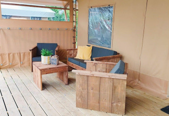 Coin salon extérieur au Glampingtent Kompact à Molengroet, Pays-Bas, avec mobilier en bois et coussins confortables.