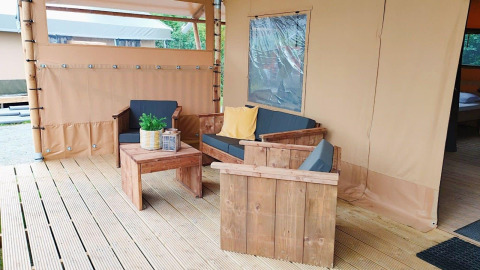 Zona de estar exterior en Glampingtent Kompact en Molengroet, Países Bajos, con muebles de madera y cojines.