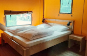 Interior view of Glampingtent Kompact at Molengroet, Netherlands, showing a wooden double bed and nightstand.