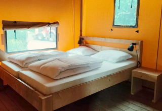 Intérieur de la Glampingtent Kompact à Molengroet, Pays-Bas, avec lit double et mobilier en bois clair.