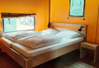 Indretning af soveområde i Glampingtent Kompact på Molengroet, Holland, med dobbeltseng og træmøbler.