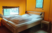 Interior de la Glampingtent Kompact en Molengroet, Países Bajos, con cama doble de madera y muebles sencillos.