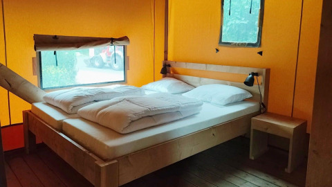 Interior de la Glampingtent Kompact en Molengroet, Países Bajos, con cama doble de madera y muebles sencillos.