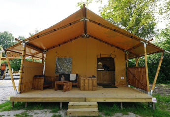 Glampingtent Sunshine-lodgen med træterrasse og siddeområde i hyggelige, grønne omgivelser.
