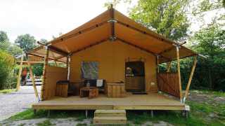 Glampingtent Sunshine Lodge mit Holzterrasse und Sitzbereich, umgeben von Natur und Bäumen.