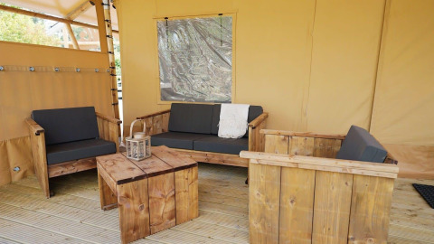 Zona de estar en Glampingtent Sunshine, Molengroet, Países Bajos, con muebles de madera y cojines.