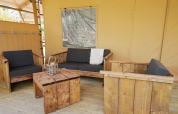 Zona de estar en Glampingtent Sunshine, Molengroet, Países Bajos, con muebles de madera y cojines.