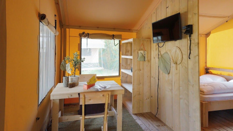 Lyst interiør af en Glampingtent Sunshine på Molengroet i Holland med træmøbler og TV på væggen.