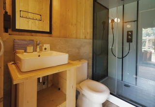 Bagno moderno con pareti in legno, lavandino bianco, WC e doccia in vetro a Glampingtent Sunshine.