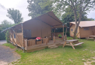 Glampingtent Sunshine al Molengroet nei Paesi Bassi, con veranda in legno e tavoli da picnic sull'erba.