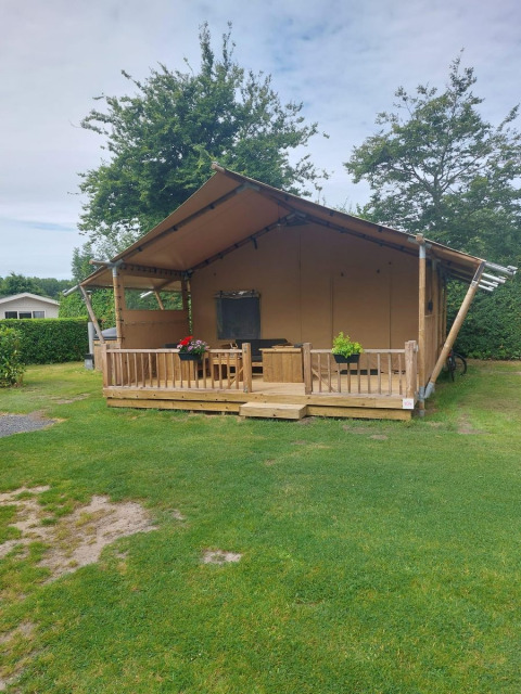 Tienda glamping Sunshine en Molengroet, Países Bajos, con porche de madera y césped verde delante.