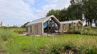 Modernes Strandhaus-Lodge mit Glasfront, Terrasse und Sitzbereichen in grüner Umgebung.