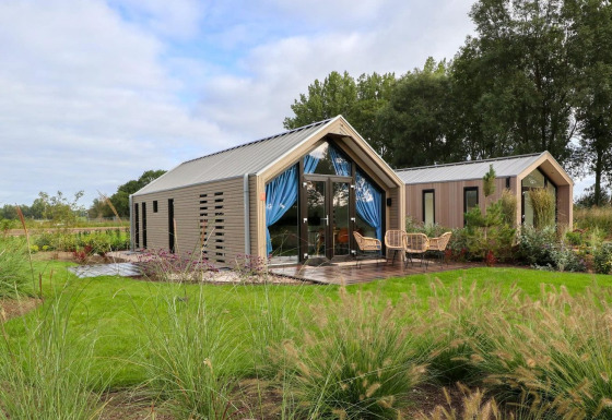 Moderne strandhus-lodge med glasfacade, terrasse og udendørs siddepladser omgivet af grøn natur.
