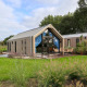 Moderne Beach House lodge met glazen gevel en buitenterras, gelegen in weelderige groene natuur.