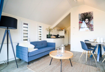 Modernes Wohnzimmer in der Beach House Lodge Bad Hulckesteijn, Niederlande, mit blauer Couch und Küchenecke.