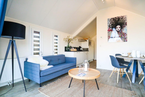 Moderne indretning i Beach House-lodge med blå sofa, spiseplads og kunst på væggen, Bad Hulckesteijn.