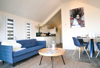 Salón luminoso y moderno en Beach House de Bad Hulckesteijn, Países Bajos, con sofá azul y arte mural.