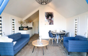 Moderne lodge woonkamer met blauwe banken, open keuken en ronde eettafel met vier blauwe stoelen.