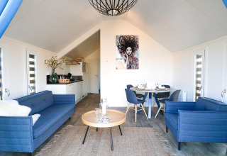 Salon de lodge moderne avec canapés bleus, cuisine ouverte et table ronde entourée de quatre chaises.
