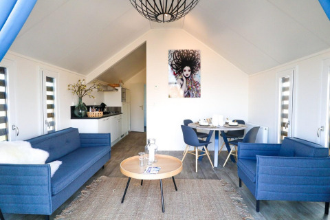 Indbydende lodge-stue med moderne blå sofaer, åbent køkken og rundt spisebord med fire stole.