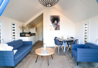 Indbydende lodge-stue med moderne blå sofaer, åbent køkken og rundt spisebord med fire stole.