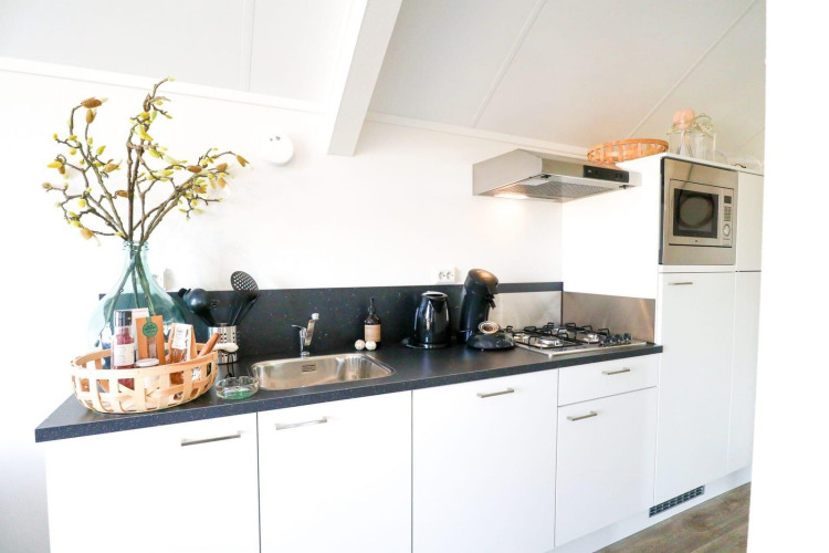 Cocina moderna y luminosa en una cabaña con armarios blancos, estufa de gas y microondas integrados.