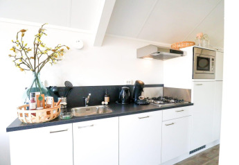 Cocina moderna y luminosa en una cabaña con armarios blancos, estufa de gas y microondas integrados.