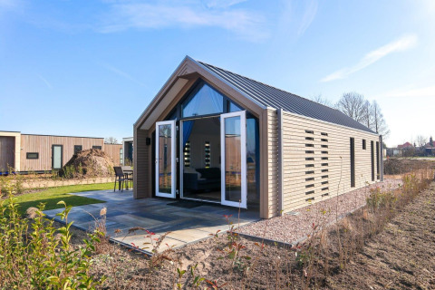 Foto van een moderne lodge met open deuren en houten gevel, gelegen in een groene, natuurlijke omgeving.