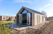 Foto van een moderne lodge met open deuren en houten gevel, gelegen in een groene, natuurlijke omgeving.