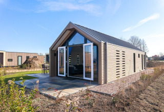 Foto de una moderna cabaña con puertas abiertas y exterior de madera, ubicada en un entorno natural verde.