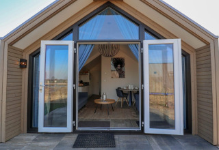 Lodge moderno con puertas de cristal abiertas y un interior acogedor, visto desde el exterior de día.