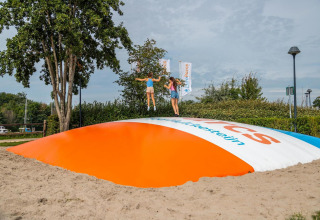 Bambini saltano su un grande cuscino gonfiabile in un’area giochi presso una struttura glamping.