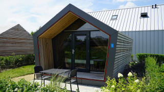 A modern Solo Retreat lodge with wood and glass exterior, small terrace, and garden on a sunny day.