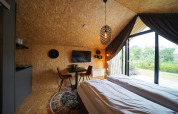 Modern ingerichte Solo Retreat lodge met tweepersoonsbed, eethoek en groot raam met zicht op tuin.