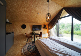 Modern ingerichte Solo Retreat lodge met tweepersoonsbed, eethoek en groot raam met zicht op tuin.