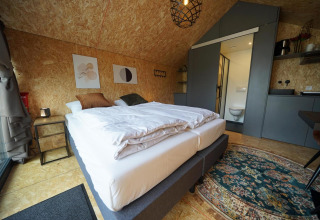 Modernes Lodge-Zimmer mit Doppelbett, Bad und Küchenzeile im Solo Retreat, Bad Hulckesteijn, Niederlande.