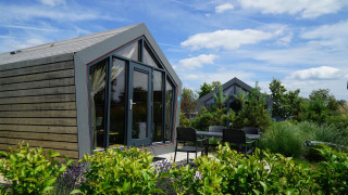 Modern Solo Retreat lodge with large windows and patio seating area, surrounded by greenery and blue sky.