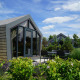 Moderne Solo Retreat-lodge med glasdøre og udendørs siddepladser, omgivet af grønne buske og træer.