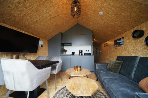 Interno di una lodge moderna con divano, tavolo da pranzo, sedie e angolo cottura al Solo Retreat, Bad Hulckesteijn, Paesi Bassi.