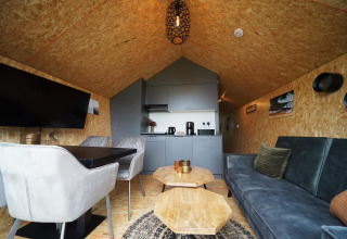 Interno di una lodge moderna con divano, tavolo da pranzo, sedie e angolo cottura al Solo Retreat, Bad Hulckesteijn, Paesi Bassi.