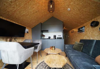 Intérieur de lodge moderne avec canapé, table à manger, chaises et kitchenette au Solo Retreat, Bad Hulckesteijn, Pays-Bas.
