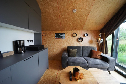 Moderne lodge in Solo Retreat, Bad Hulckesteijn, Nederland, met grijze zetel en keukenhoek.
