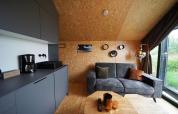 Moderne lodge in Solo Retreat, Bad Hulckesteijn, Nederland, met grijze zetel en keukenhoek.