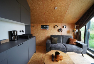 Moderne lodge in Solo Retreat, Bad Hulckesteijn, Nederland, met grijze zetel en keukenhoek.